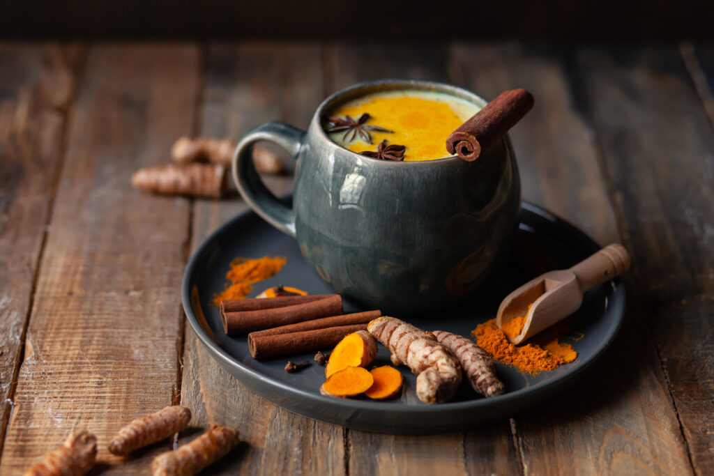 Golden milk in grey mug. Turmeric latte made with curcuma, cinnamon, anise. Healthy hot winter drink, natural, organic beverage. Close up, front view. Wooden rustic background. Raw roots as decor